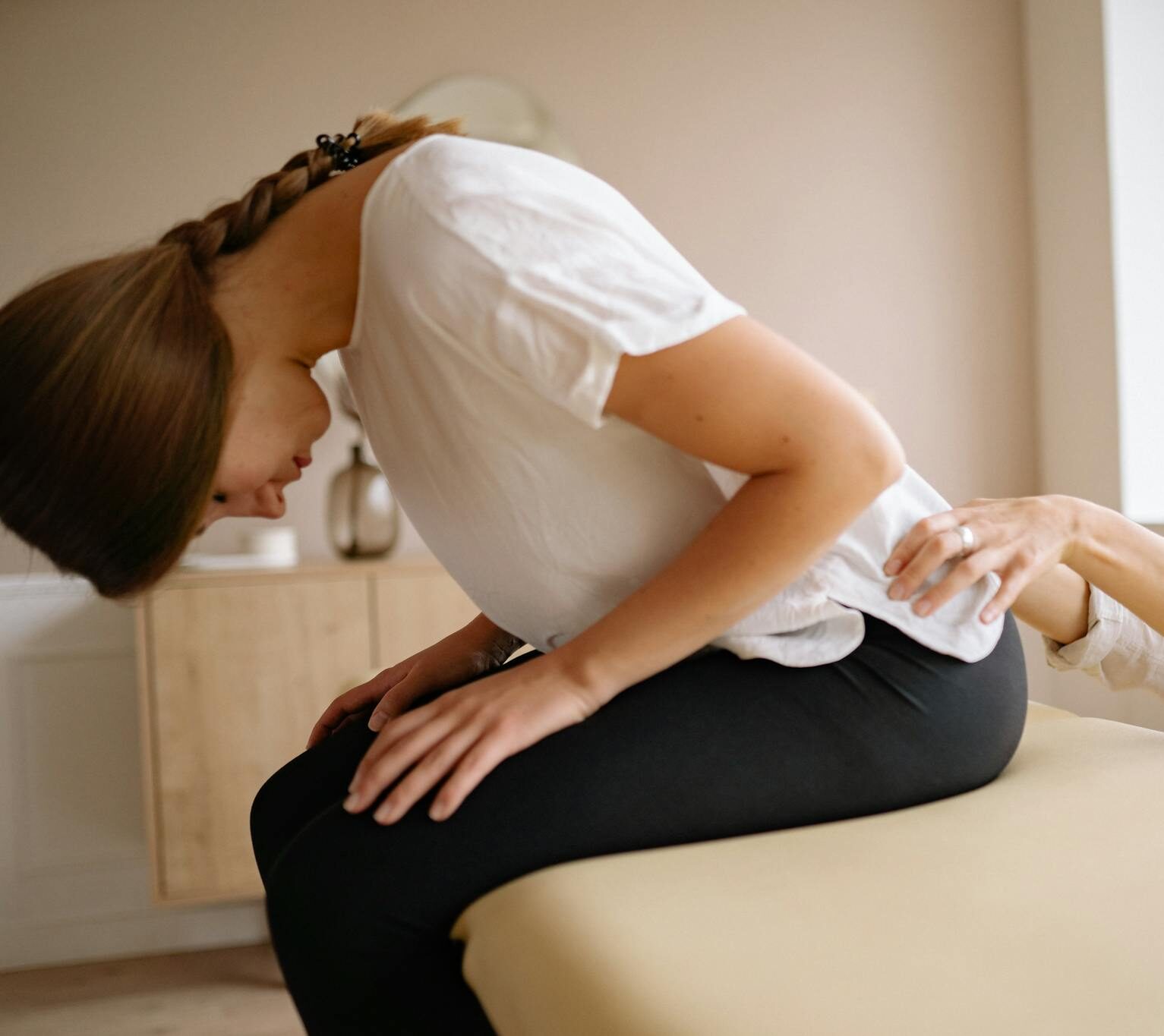 A therapist stretches a patient's back during a physical therapy session indoors.